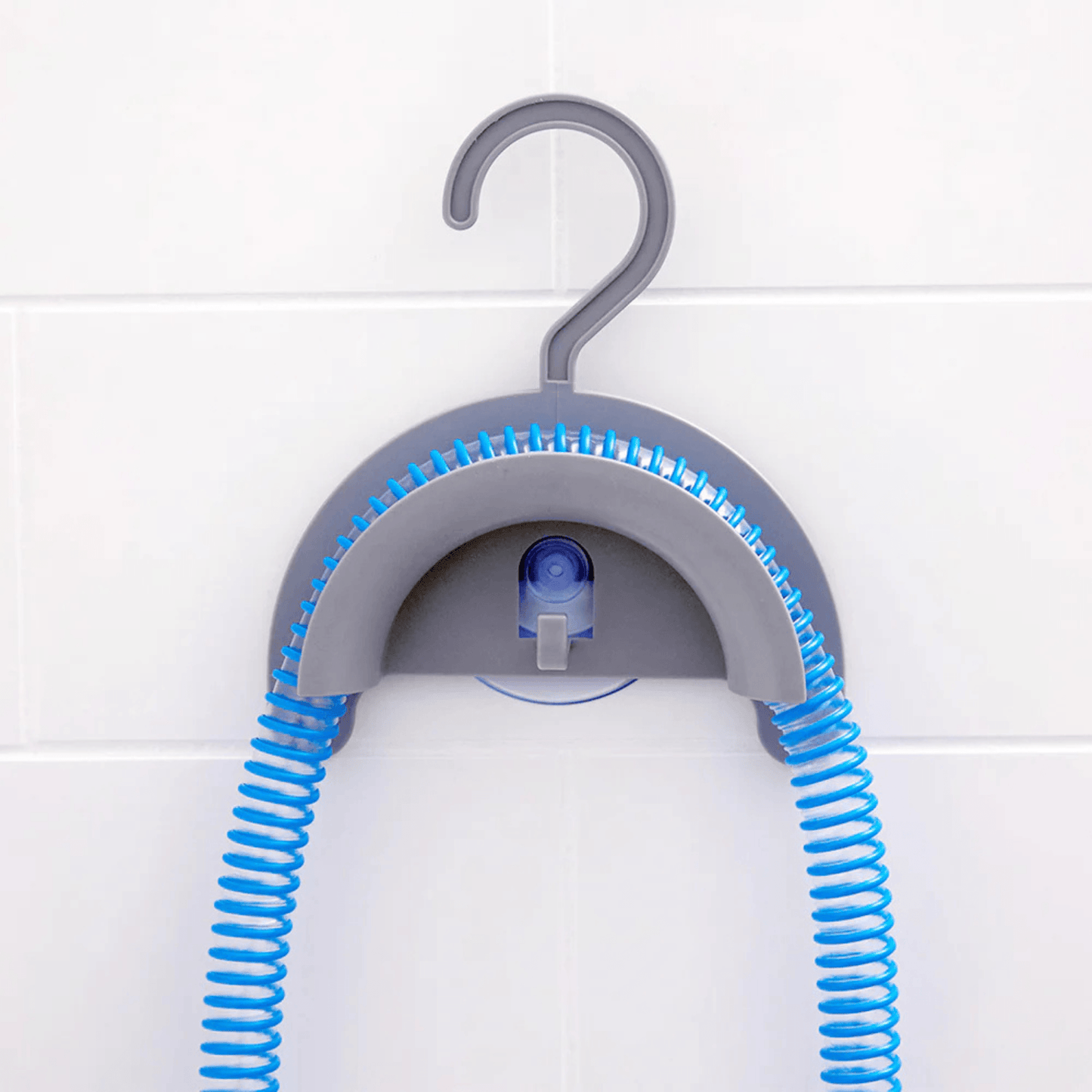CPAP Soap Hose Hanger mounted to a wall via suction cup with a blue CPAP hose draped over the curved body and both ends hanging down to air-dry