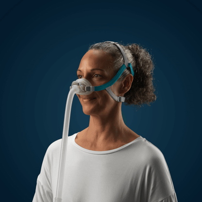 A smiling female user wearing the Fisher & Paykel Nova Nasal Mask against a dark blue background, showcasing the low-profile design and clear field of view.