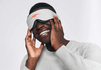 This is a young man wearing the manta sleep mask over his eyes and smiling. 