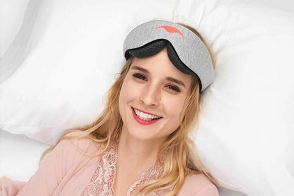 A woman wearing the manta sleep mask and smiling after waking up and the mask is on her forehead. 